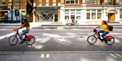 Two women using Santander Cycles, cycling along Cycleway 2 - a seperate cycle lane next to the road