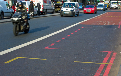 road with red route parking bay indicated by red dotted lines. cars and a motorbike are in a seperate lane